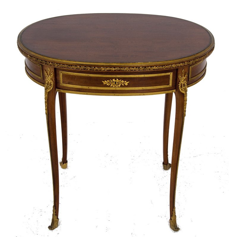 FRENCH ORMOLU MOUNTED MAHOGANY OCCASIONAL TABLE: the lock signed "SORMANI PARIS 134 Bd. HAUSSMANN" the oval top bound in a gilt bronze foliate design; the frieze having a single drawer and rectangular gilt bronze mounts on four sides; on four thin c