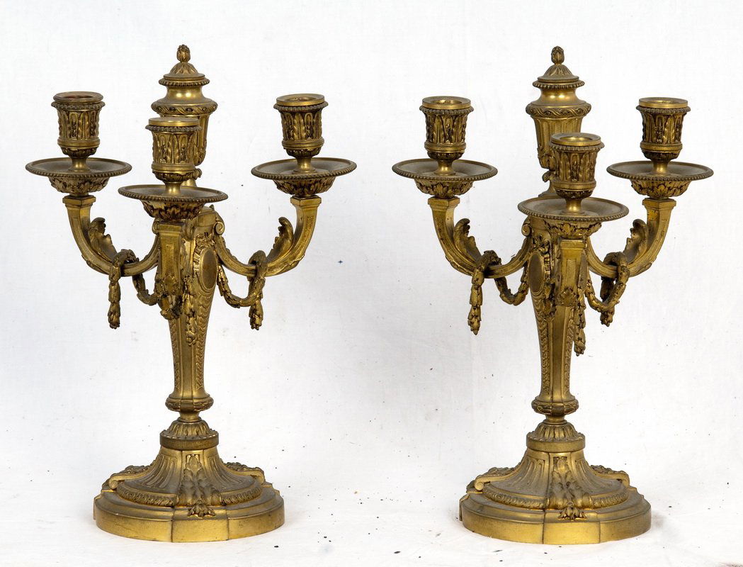 PAIR OF FRENCH GILT BRONZE CANDELABRA: in the Louis XVI style, each having three lights draped with a garland and centering an urn-form finial above a column with cartouche designs, on a round fluted foot; with Susse Freres foundry mark 14
