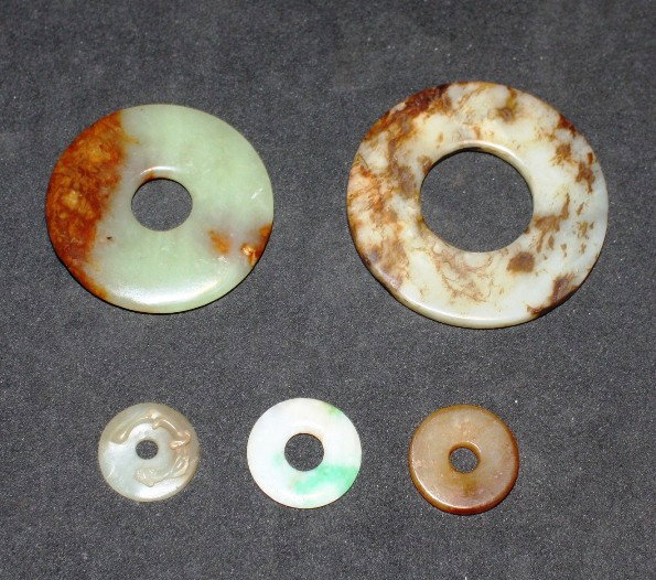 A group of four jade bi discs: of celadon and russet archaistic colour, comprising three plain ones, a smaller one carved with a dragon, and a small jadeite disc The largest, D. 60mm Provenance: From the Leo Walker Tattersfield Col