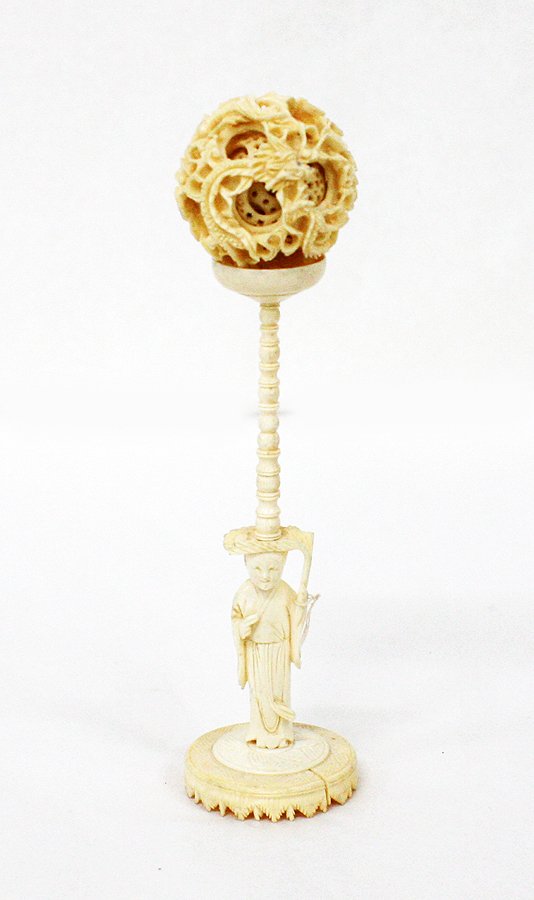 Small Cantonese ivory puzzle ball and stand: 19th century The largest concentric pierced ball carved with two dragons amongst clouds, containing balls pierced with a geometric pattern, the stand carved with a figure holding a fly whisk. H. 200mm