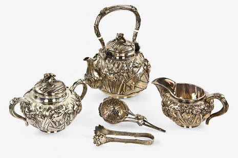 Japanese export silver tea service: Meiji period (1868-1912), decorated with repoussé iris blossoms and hammered background texture, comprising lidded teapot, lidded sugar bowl, creamer, tongs and strainer, marked Jungin. W. 180mm