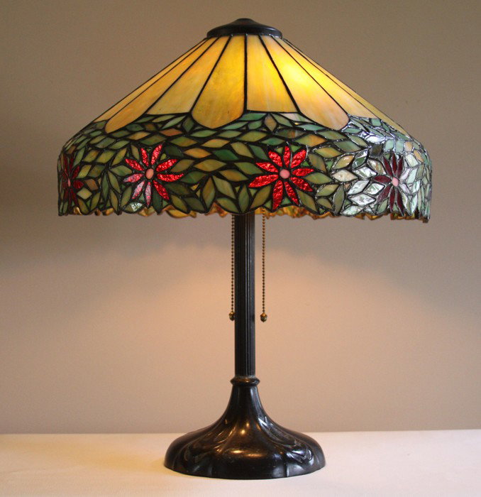 Handel 18" "Poinsettia" leaded glass lamp: Handel 18" "Poinsettia" leaded glass lamp. Poinsettia flowers are a fiery red granite backed glass with mottled and striated green panel glass above. Base has two original Hubbell sockets operated by