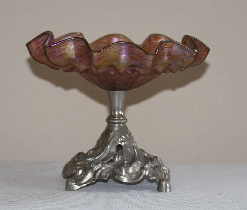 Loetz oil spot compote in Metal Art Nouveau Stand: Loetz oil spot compote supported by a French Art Nouveau reticulated and nickel plated stand. Exceptional condition. Glass having no chips, or cracks. Estimate $150-$250