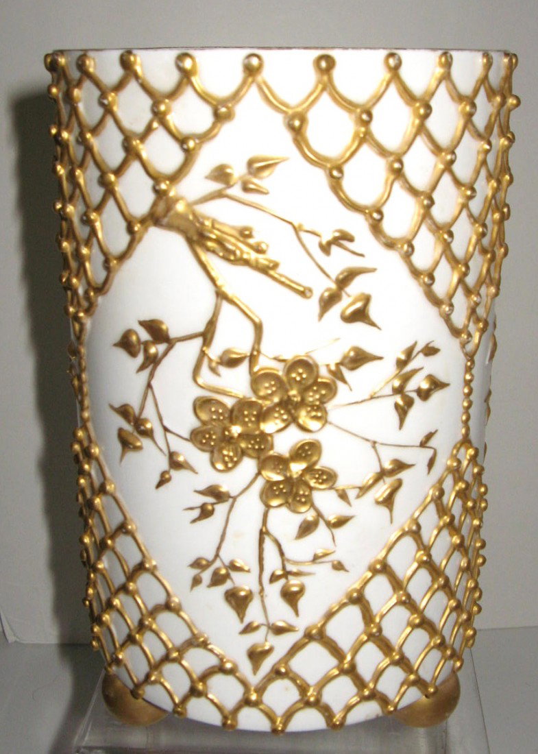 Lotus Ware porcelain vase,: cylindrical form in white porcelain decorated with gilt netting forming diamond medallions of Gingko branches, adorned with three ball feet, signed Lotus, 8" ht. Condition: good no damage