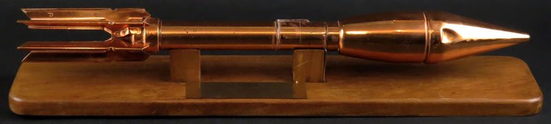 WWII Wall Mounted Copper Plated Bazooka Missile. High: WWII Wall Mounted Copper Plated Bazooka Missile. High Explosive Rocket Propelled One Man Anti-Tank Missile Range 100 Yards 59mm Caliber Mounted on Wooden Stand. Overall Measures 22-1/2 Inches. Has Art