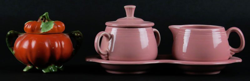 Pink Fiestaware Cream Pitcher and Covered Sugar on: Pink Fiestaware Cream Pitcher and Covered Sugar on Matching Tray. Signed. Together with an Unsigned Figural Tomato Covered Sugar with some Flaking. Undertray Measures 10 Inches Long. Shipping $20.00