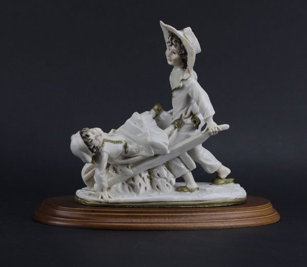 Vintage Capodimonte Wheelbarrow Boy with Girl on Wooden: Vintage Capodimonte Wheelbarrow Boy with Girl on Wooden Base. Artist Signed. Some Residue to Surface or else Good Condition. Measures 9-1/2" H by 11" W. Shipping $45.00