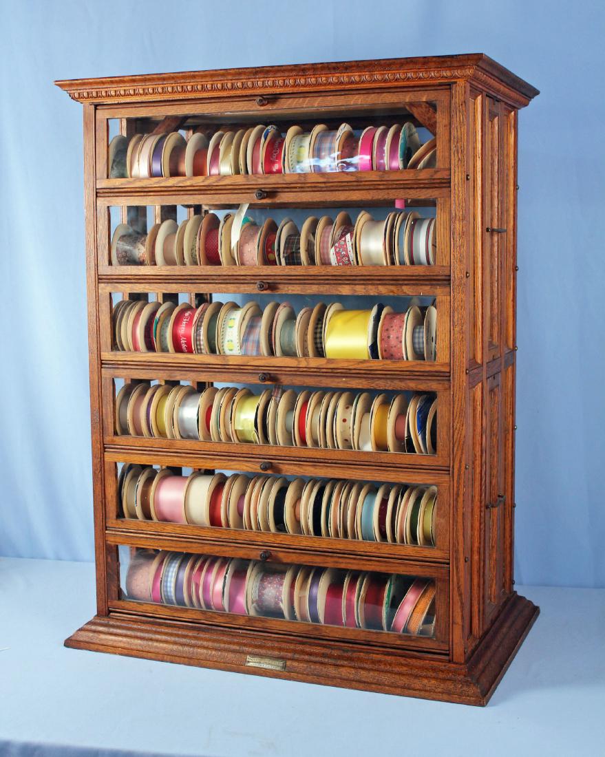 A.N. Russell & Sons Oak Three Tier Ribbon Cabinet: A.N. Russell & Sons Oak Three Tier Ribbon Cabinet with 18 ribbon compartments. Cabinet center section slides out with two drawer. End tiers have six folding doors. Cabinet has the original manufacture