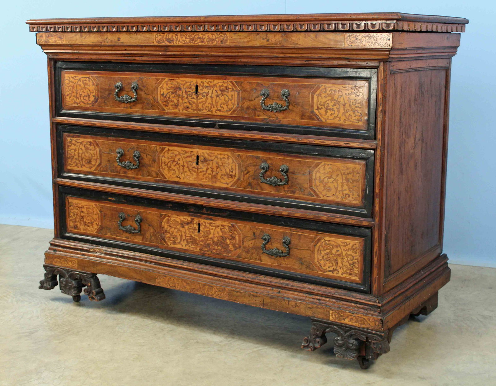 North Italian Marquetry Commode 18th C.: A North Italian Walnut and Marquetry Commode, Late 17th or Early 18th Century. Commode has three drawers with cast cupid mask pulls below hidden drawer under rectangular top and scrolled carved front 