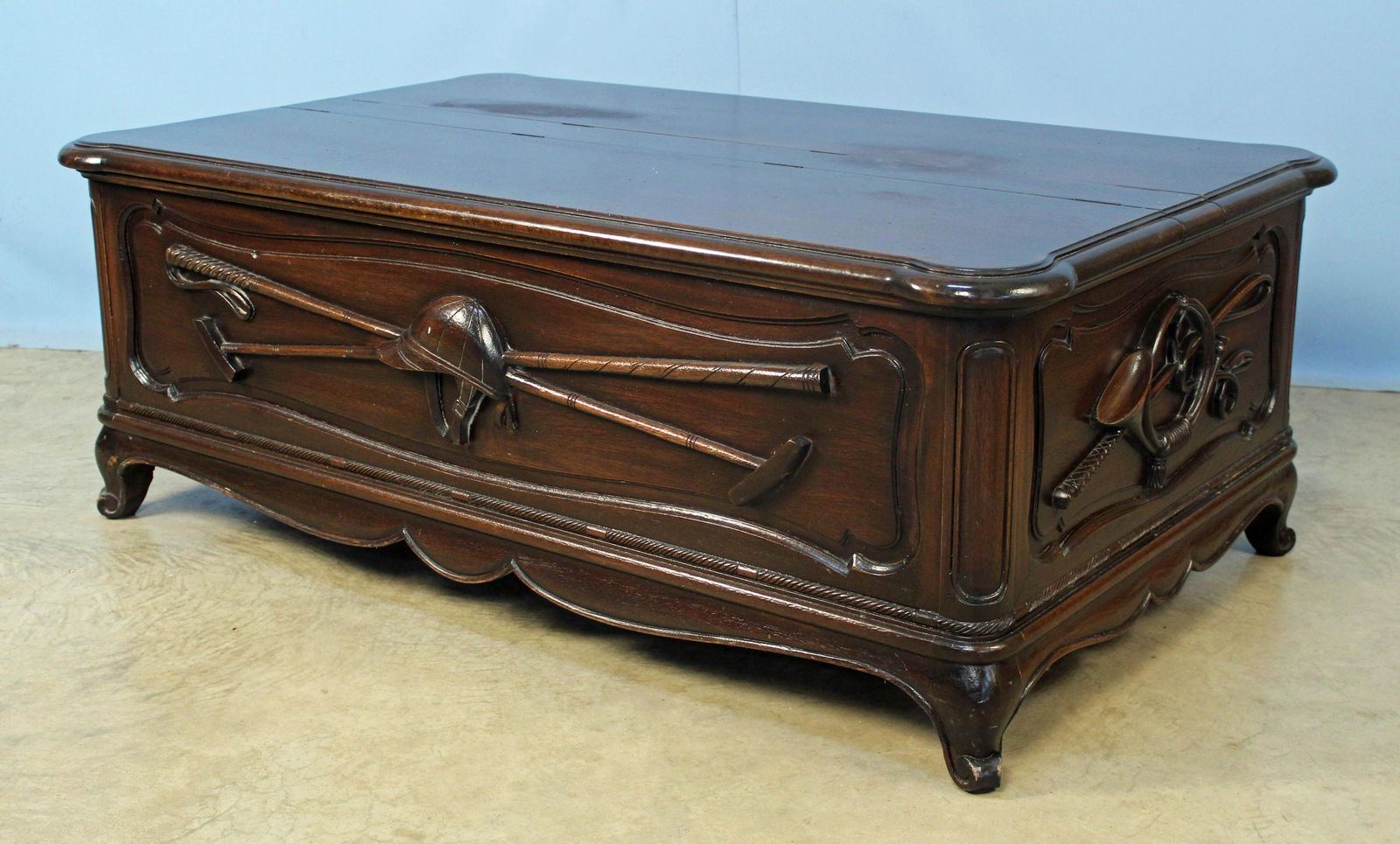 Mahogany Coffee Table with Lift-Top Storage: Mahogany Coffee Table with Lift-Top Storage. The table has relief carved Polo hat and mallet and fox hunting horn and whip. The top has two lift lids for access to storage. The finish is a heavy craqu