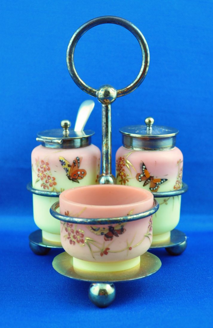 Thomas Webb and Sons Condiment Set: Burmese 3 piece condiment set crafted by Thomas Webb & Sons in silver plate stand, the artist painting a cascading sprig of flowers and butterflies upon the acid surface. The height of the 2 taller pi