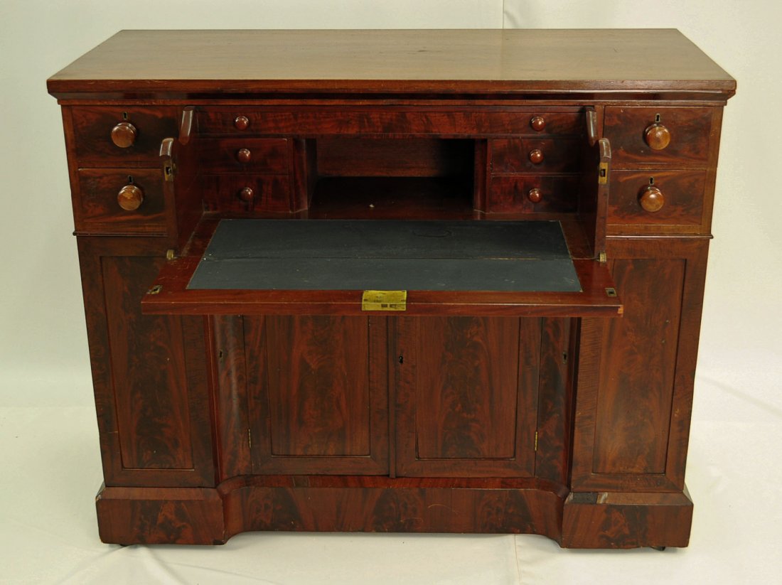Empire Crotch Mahogany Butlers Secretary Desk: Empire crotch mahogany butlers secretary desk circa 1830. Drop front drawer section pulls out to reveal desk section with writing area and pigeon holes. Four drawers flank desk section above four door