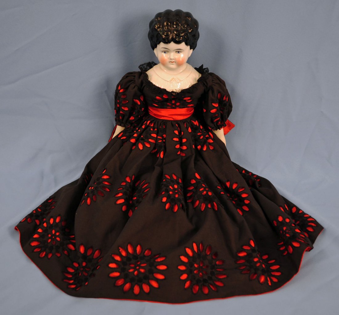 24" China Head Doll W/ Molded Collar: 24" China Head And Shoulder Doll W/ Molded Collar. Marked, "Marion," on shoulder plate. Doll has cloth body, black hair, low brow, blue eyes, molded collar, and wears a black eyelet dress with red tri