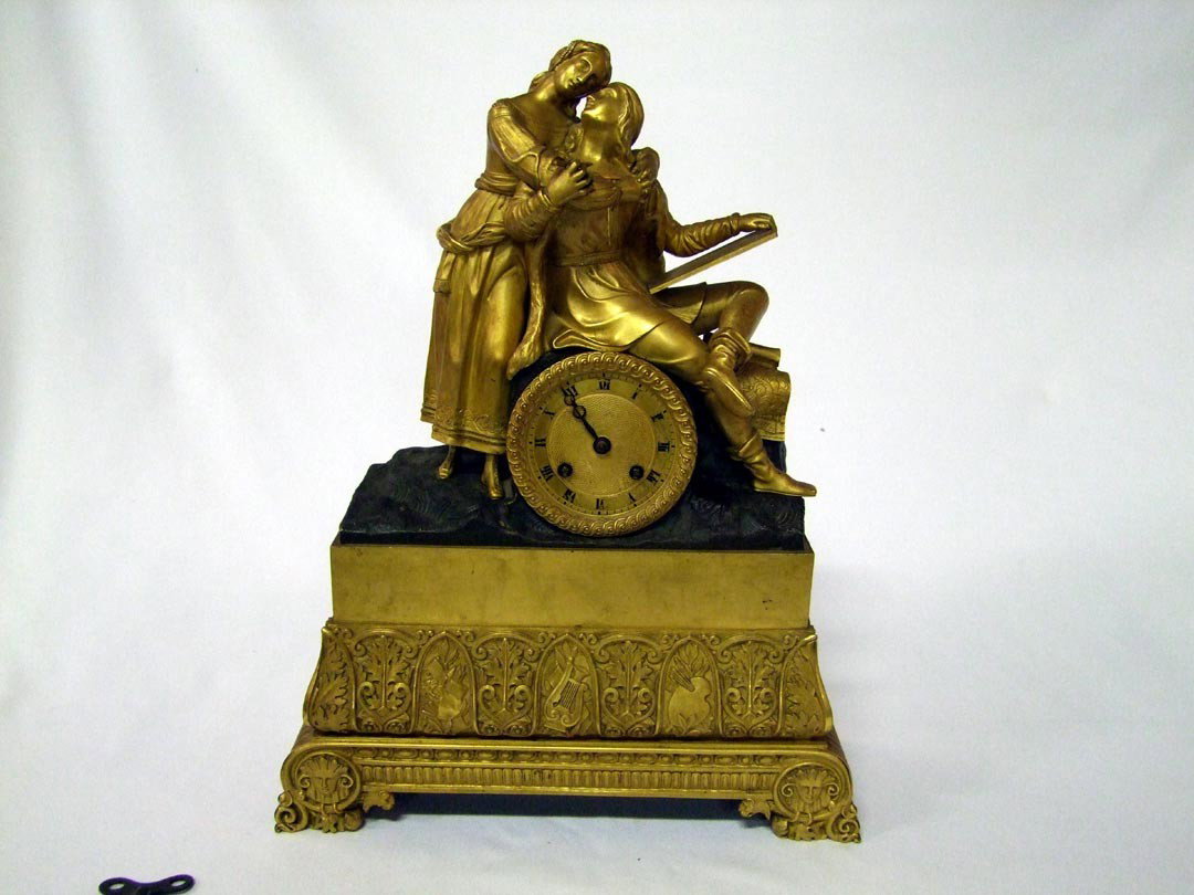 Empire Bronze Figural Clock: Standing woman with her arms around a young seated scholar. A band on the base has cartouches depicting the arts, alternating with an anchor design with leaves. Female faces on the front feet. No Make