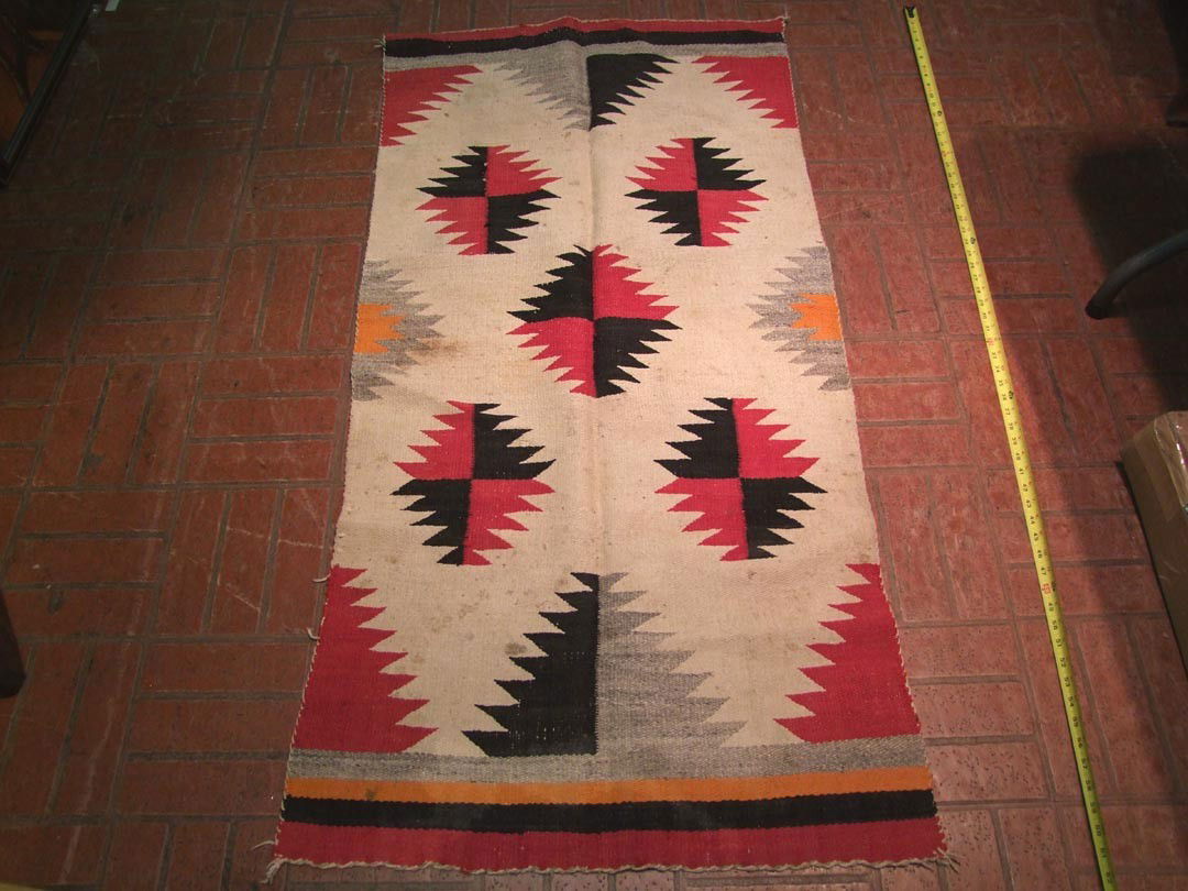 Navajo Rug: Hand-made 1910 Navajo rug with red, dark brown, grey, cream and orange. Scattered spots. 30" x 59".
