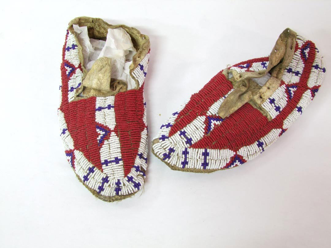 Beaded Sioux Or Crow Moccasins: Possibly Crow Indian, 1890 - 1910 beaded with red, cobalt and white glass beads, sinew stitched. Minor bead loss around toes and soles have been repaired with heavy thread and cord. 10" long.