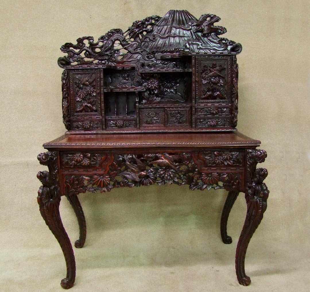 Oriental Carved Desk: 19th century elm desk carved with dragons, birds and flowers. The base stands on four carved legs with a pierced carved apron. The back has climbing dragons flanking carved doors and the center area o
