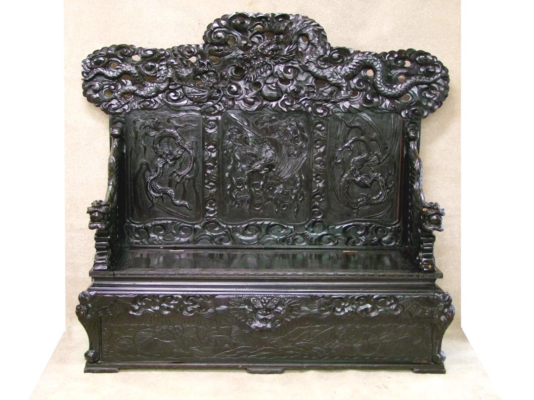Oriental Temple Bench: 19th century carved ebonized bench with three panels in the back, flying dragons flanking a phoenix bird. At the crest are two fighting dragons and dragons form the arms. Hinged lift lid storage compa