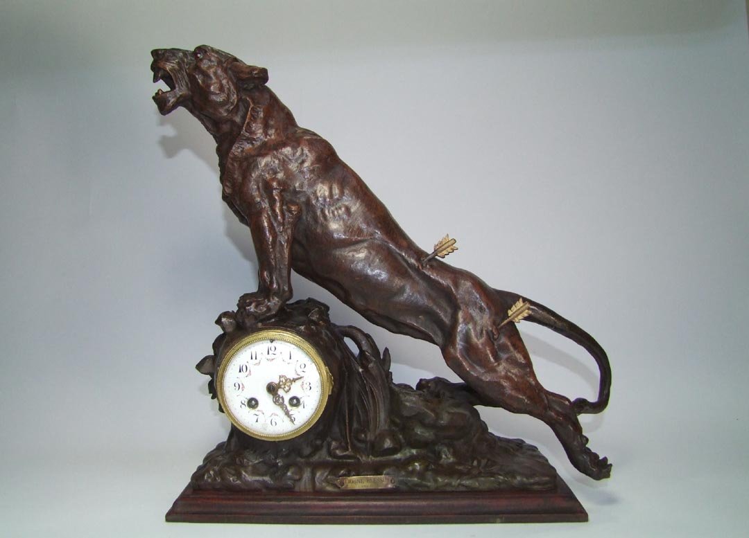 Wounded Lioness Clock: Bronzed spelter clock with plaque that reads "Lionne Blessee Par Omerth" showing a hunted lioness that has been injured by two arrows. She has faceted red glass eyes and a repaired tail. Porcelain dia