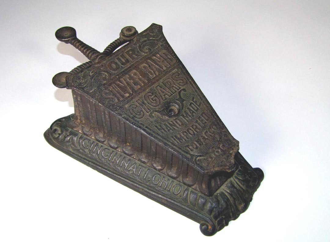 Mechanical Cigar Cutter: Key wind cast iron counter cigar cutter by A. Davis Sons & Co. in Cincinnati, Ohio. Advertising on top reads," Our Silver Band Cigars Hand Made Imported Tobacco". Once it is wound up then the customer