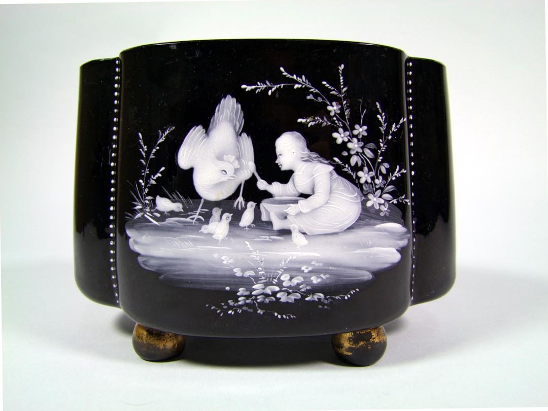 Mary Gregory Black Vase: Black glass vase, raised on four ball feet, with white decoration of a young girl with a chicken and chicks. Worn gold. 8" x 5" x 5 1/2" high.