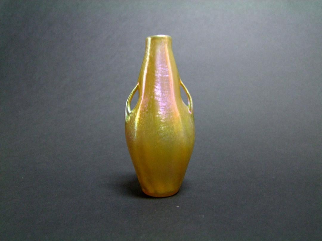 Gold Tiffany Cabinet Vase: 4 1/4" cabinet size Tiffany gold vase with handles signed L.C.T. Favrile 1411 C. Soft gold iridescence with pink and green highlights. Very fine condition with one small burst bubble near the base.