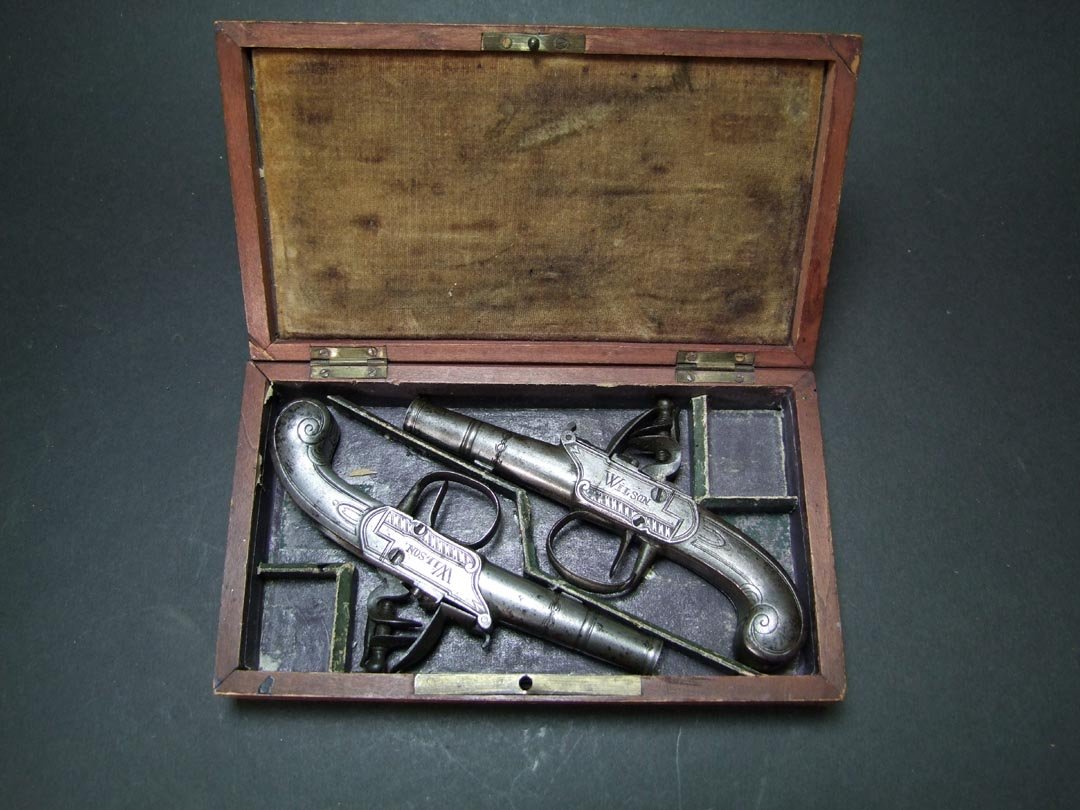 1785 - 1810 Dueling Pistols: Marked Wilson on one side and London on the other with English hallmarks under the round barrel. Engraved trigger guard. 6" overall. Black powder. Key locking case with no key.