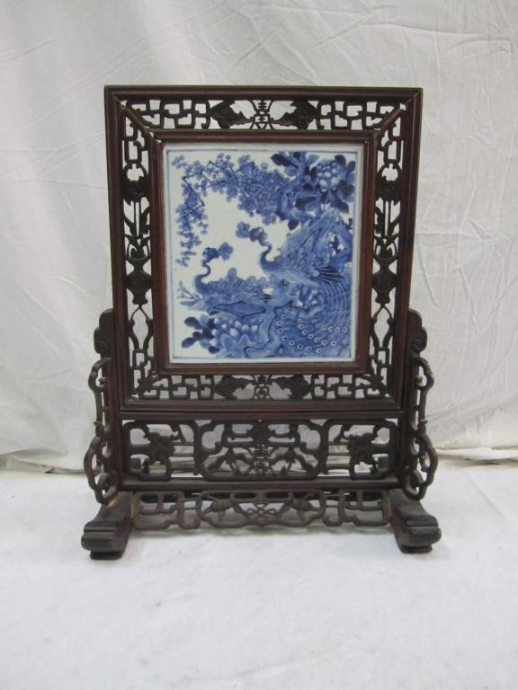 Chinese Blue and White Porcelain Table Screen: Inset blue and white porcelain plaque in teak carved frame stand with bat decor. 18 w X 23 tall.