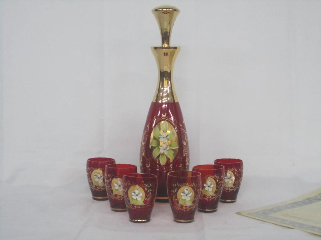 Viennese Carafe and 6 Cordials: hand-painted ruby glass and gilt carafe with gilt stopper (H: 12") and 6 matching cordial shot glasses (H: 2 ½"), with COA