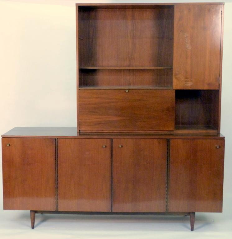 Mid-Century John Stuart 2 Part Cabinet: Upper section with fall front bar and upper right door. Lower section having 4 doors on splay leg base. Good to very good condition. 19D X 72W X 32(base) and 74(cabinet top). 8 East 83rd Street Estate