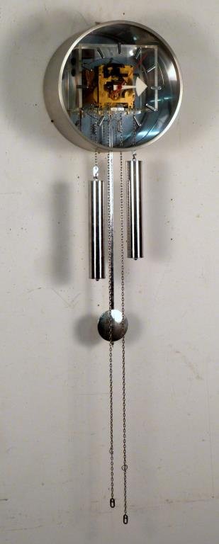 George Nelson for Howard Miller Wall Clock: Brushed silver colored metal with transparent dial face revealing brass works, weights, chain, and pendulum pendant. 12" D:; 31" L (including pendulum).