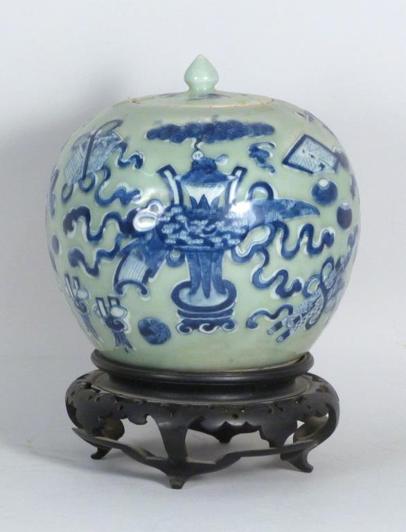 Chinese Covered Ginger Jar on Stand: Porcelain, celadon ground with blue and white vases and jues amid floral scroll, on wood stand. 9" H X 9" D (not including stand). Chip to lid, small chips and hairline to rim.