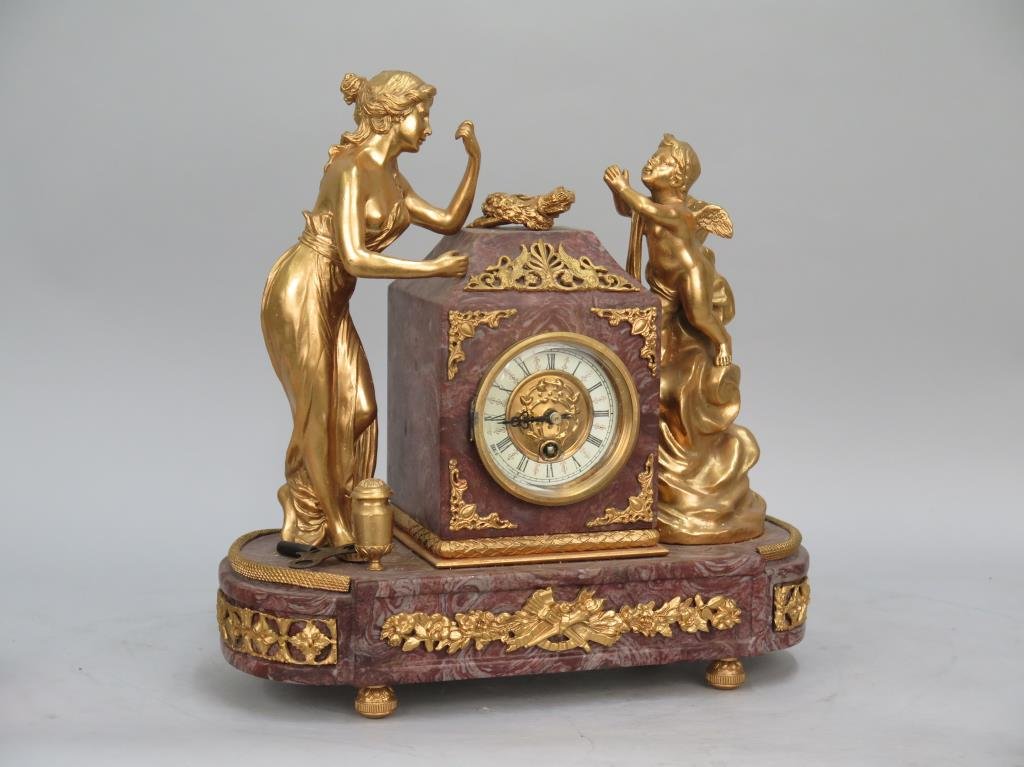 Marble and Ormolu Mantel Clock: A fine lady and putto flank clock casing. Ormolu accents. Signed Sauvgok at base of putto. With key. Chip in rear right marble top of casing. Slight lift in right ormolu trim above base. 14W X 7"D X 1