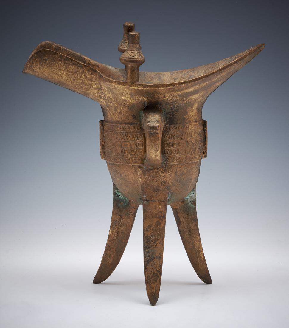 Chinese archaic bronze wine vessel: Chinese archaic bronze wine vessel, oval asymmetrical shape with two finials on the rim, one handle on the side with animal face, the body encircled with a band of yunwen designs, tapering tripod legs