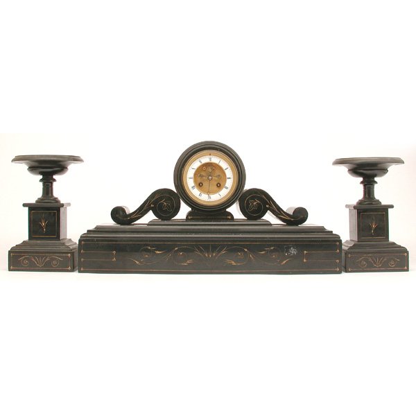 French Black Slate Mantle Clock & Garniture: CLOCK. French black slate mantle clock with two urn garniture, each decorated with incised floral scrolls decorated with gold color, two scrolls support the central clock with enamel face with a gilt 