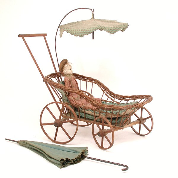 American Victorian Toy Carriage, Doll & Parasol: LOT. Group of American toy items; a wicker baby carriage with push handle and an umbrella overhead, there are three bedding pieces that match the umbrella, a wax doll in original Victorian dress, she 