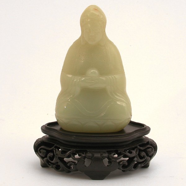 Chinese Carved Jade Guanying & Wood Stand, early: CARVING. Chinese carved jade Guanying & wood stand, early 20th c. The Bodhisattva seated on a lotus pedestal wearing long robe with cowl over the head with eyes downcast in a serene expression and bot