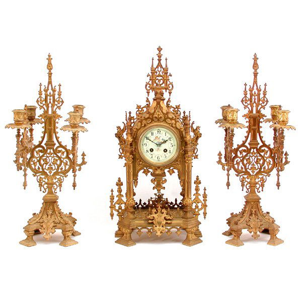 Dore Case Gothic Garniture Clock Set: GARNITURE. Three piece 19th c. Gothic Revival garniture set, in gilt intricate bronze clock with porcelain dial decorated with winged putti, with time and bell strike French movement, matching pendulu