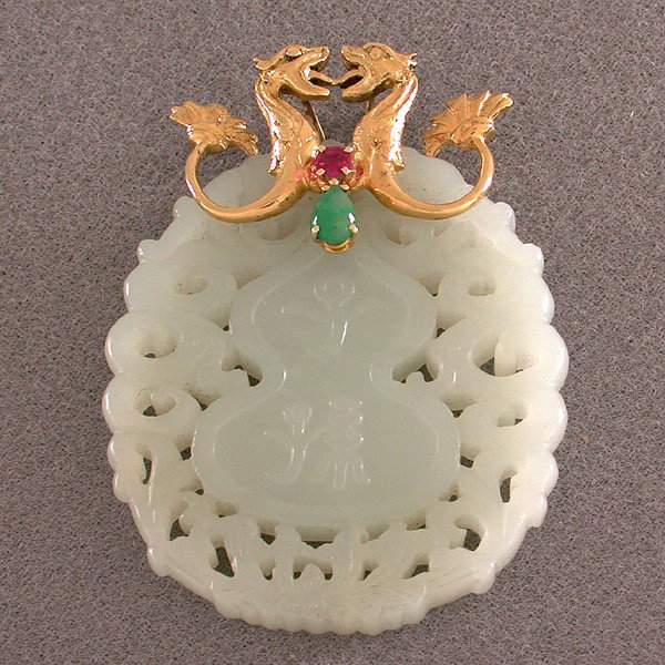 18 Karat Gold, Mutton Fat Nephrite Jade & Ruby: PENDANT. Carved, pierced oval Mutton Fat Nephite Jade pendant 5.0cm - 6.3cm, a bail of two gold sea serpents with a faceted ruby and jadeite cabochon.