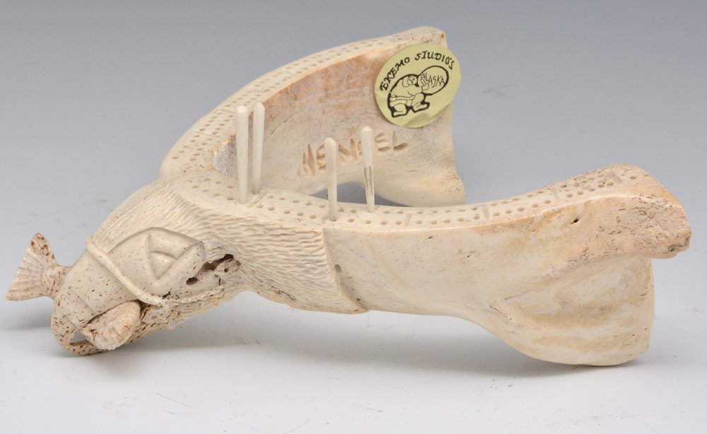 Kent Heindel bone cribbage board: Kent Heindel bone cribbage board with carved eagle with fish in its beak, signed "Heindel", retains "Eskimo Studios, Alaska" sticker. 6 3/4" x 7". Very good original condition.