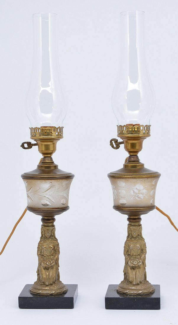 Pair Of Bronze Figural Kerosene Lamps (Electrified): Pair of bronze figural kerosene lamps (electrified) with frosted decorated glass font and ebonized wood base. Very good condition. 24"h to top of chimney.