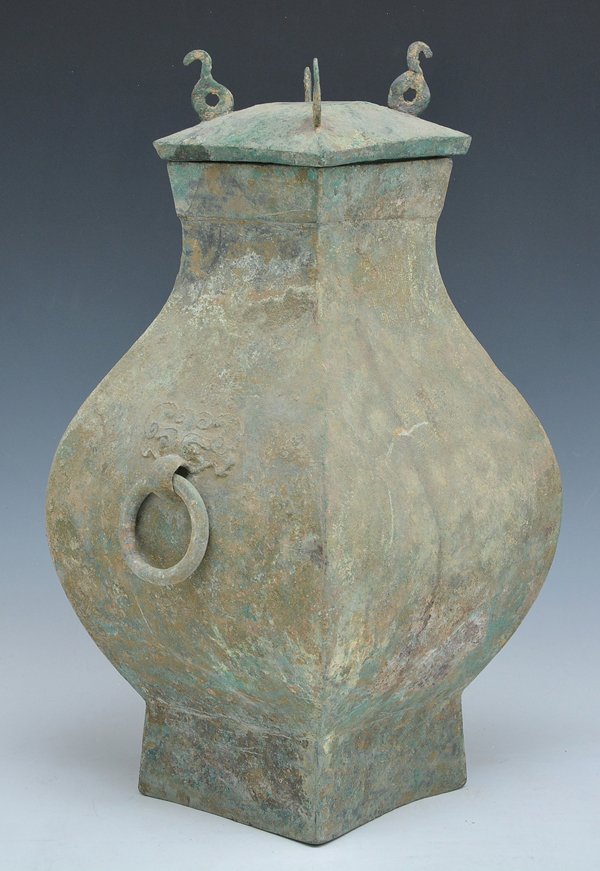 Chinese Bronze Hu Form Vessel, Han Dynasty: Chinese archaic bronze Hu form vessel, Han dynasty, of square baluster form on a flared foot with ring mask handles and lid. Appx 16 3/4"h x 8 1/4"sq.