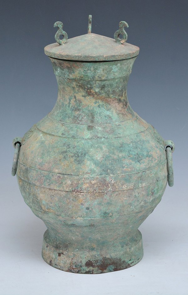 Chinese Bronze Hu Form Vessel, Han Dynasty: Chinese archaic bronze Hu form vessel, Han dynasty, of round baluster form with ring decoration on a flared foot with ring mask handles and lid. Appx 13"h x 8 1/2"d.