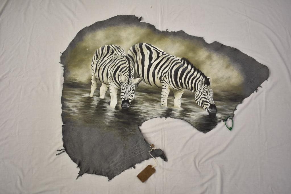 Elephant Ear Zebra Painting by B. Marshall: Painting of zebras is on an Elephant ear by Belinda Marshall. Has original green tag for registration purposes. Leather tag states " M O'Banion ELE EAR OUT HEIGHT 30". Measures 54" wide and 43" tall.