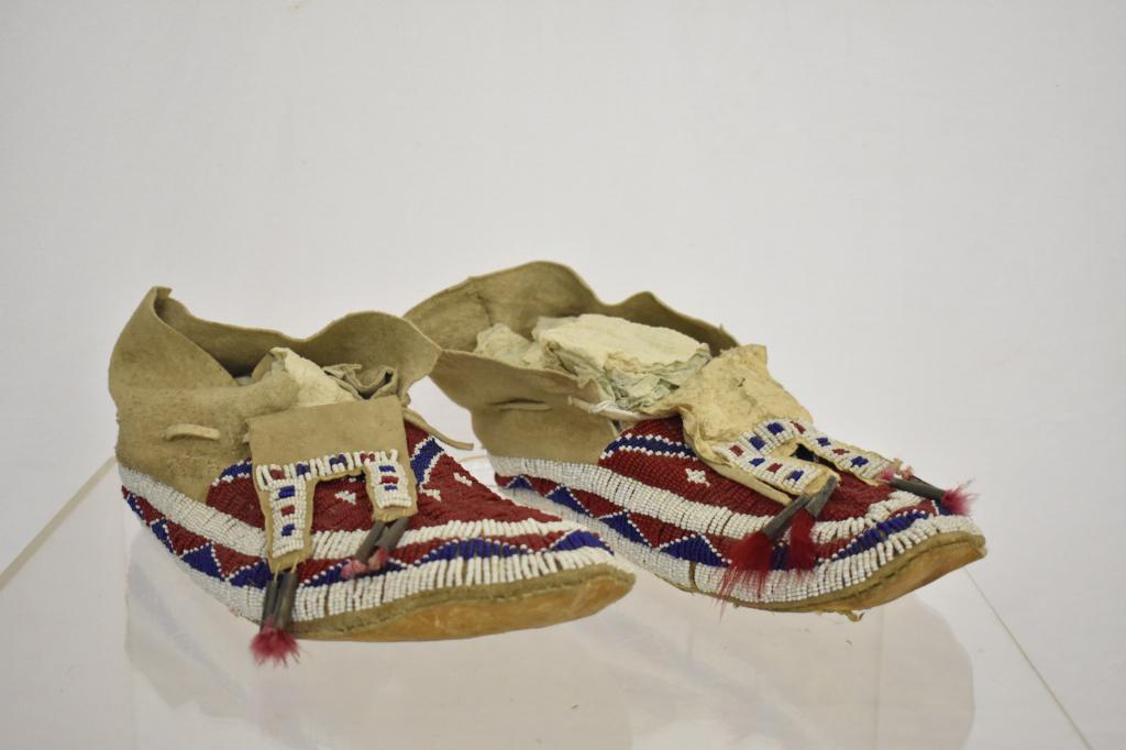 Northern Plains Native American Beaded Moccasins: Early 1900's men's moccasins. Red, white & blue bead with tin tubes holding tassels. Measures 11". Condition very good. Dr. Michael O'Banion Estate.