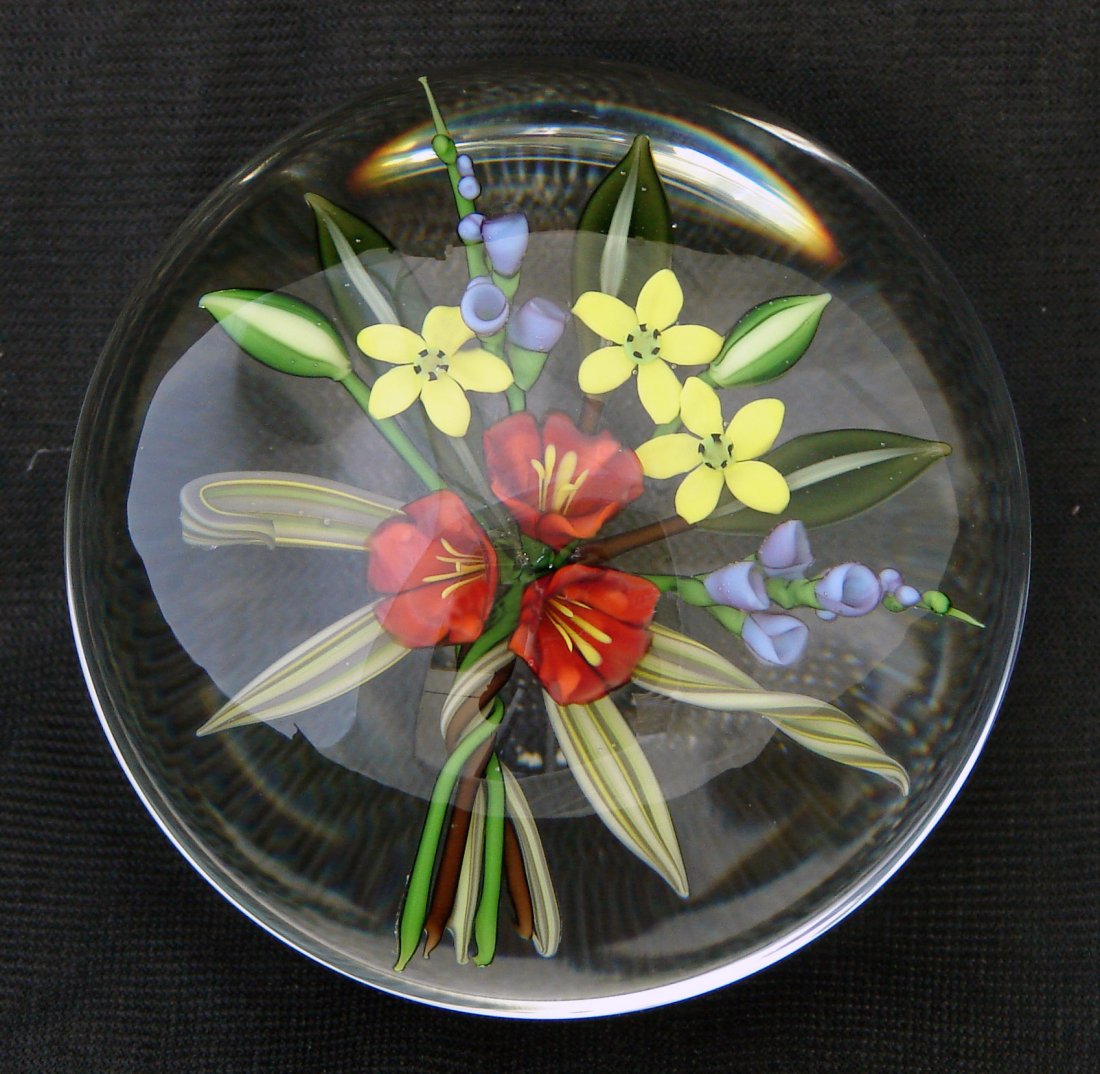 Chris Buzzini Paperweight 1987 Flowers: Chris Buzzini paperweight, signed and dated "Buzzini '87 RAB 53". 1987 Description: A bouquet of red, blue and yellow flowers with leaves of each plant is set over a clear ground. Chris Buzzini “aza