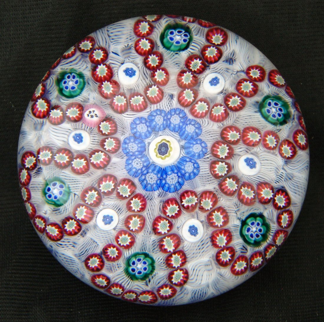 1973 Baccarat Paperweight Millefiori: 1973 Baccarat paperweight with a date cane that reads "B1973" Description: Red, white, blue and green millefiore in a garland design on a bed of white scrambled latticinio on a cobalt blue ground. Loo