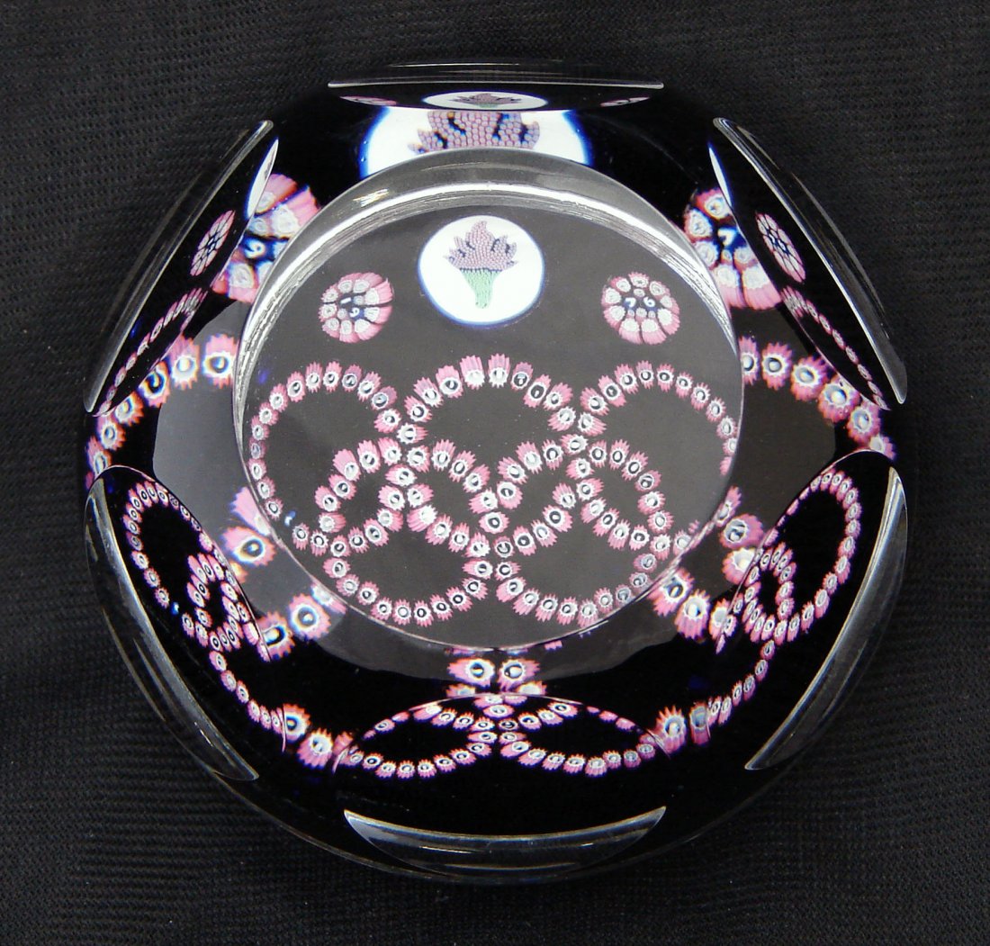 Olympics Themed Whitefriar Paperweight 1976: "Olympics" themed Whitefriar Glass Paperweight with pink patterning on a blue background and squared edges. Dated 1976 on front with "19" on the left and "76" on the right. 2 1/2" height by 3 1/2" wid