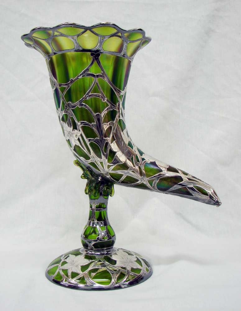 Large Green Loetz Type Glass Cornucopia Vase Sterli: Cornucopia shaped glass vase with sterling silver overlay and iridescent finish to the glass. No markings. 12" height by 9" across. Good condition with cracks along the glass base and one silver flowe