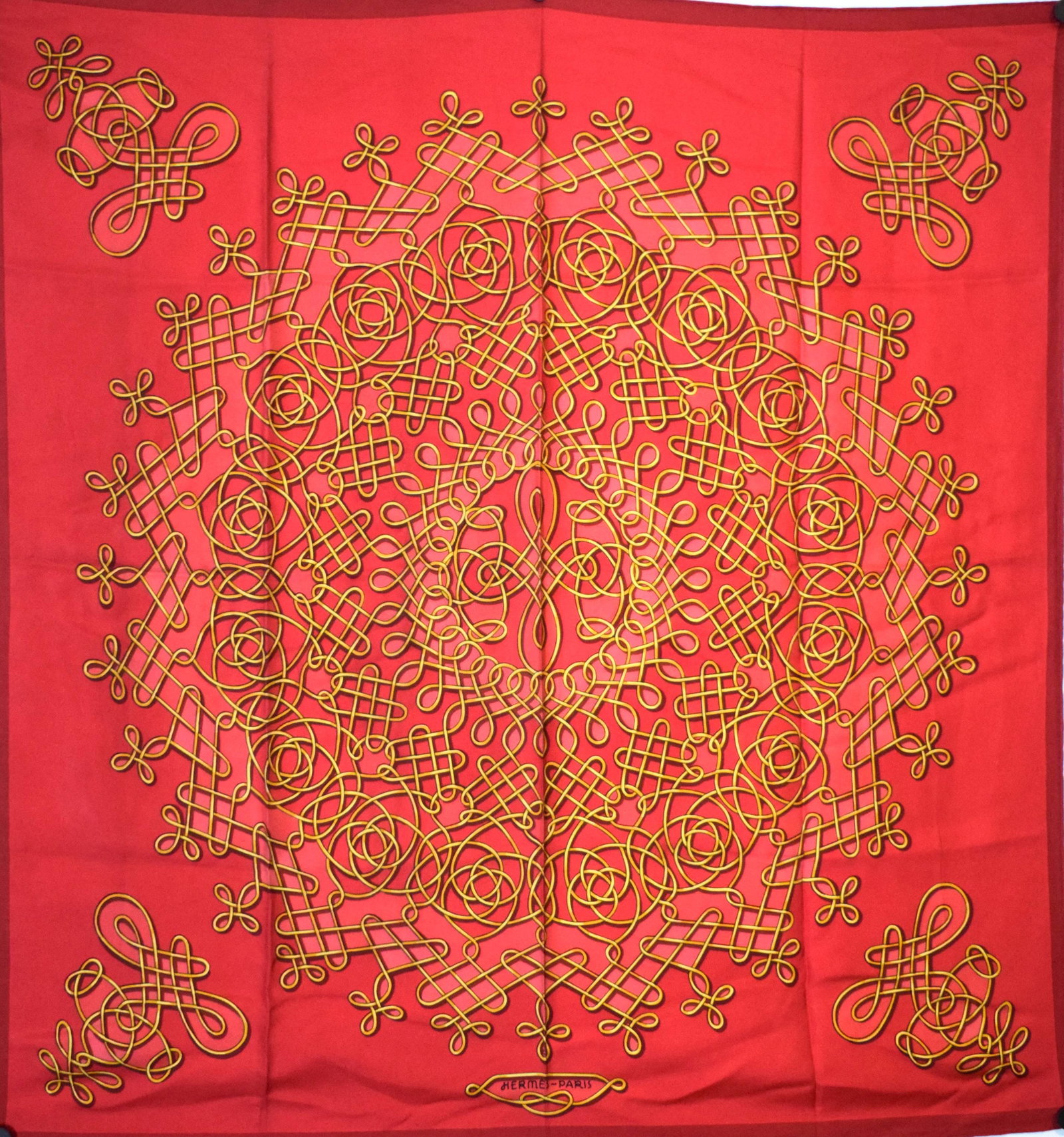 HERMÈS: Carré en twill de soie imprimé à décor de volutes sur fond rougeDim : 85 X 85 cm(petites salissures)